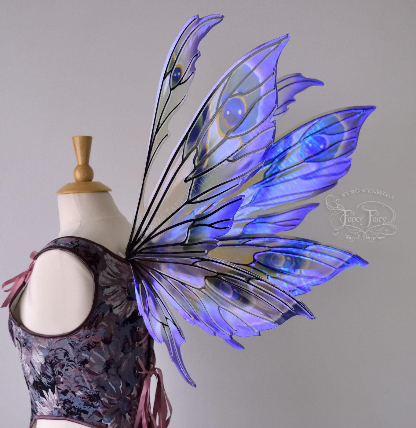 Large transparent fairy wings with antennae have peacock 'eye' accents painted on violet iridescent film with black veins, worn on dress form, back 3/4 view