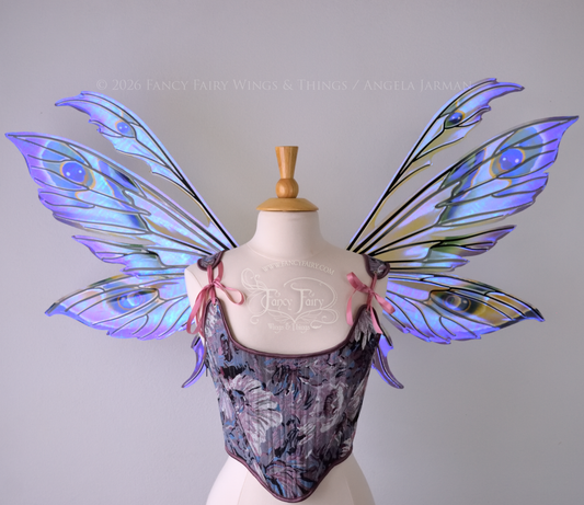 Large transparent fairy wings with antennae have peacock 'eye' accents painted on violet iridescent film with black veins, worn on dress form, front view