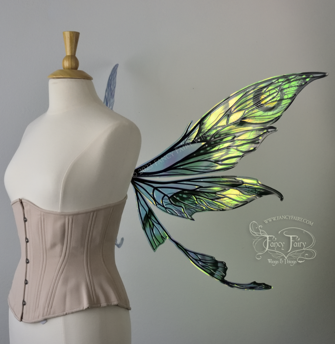 Right side view of large green, gold & black painted iridescent fairy wings with black veins. Upper panels are elongated with pointed tips, a ‘tail’, lots of vein detail