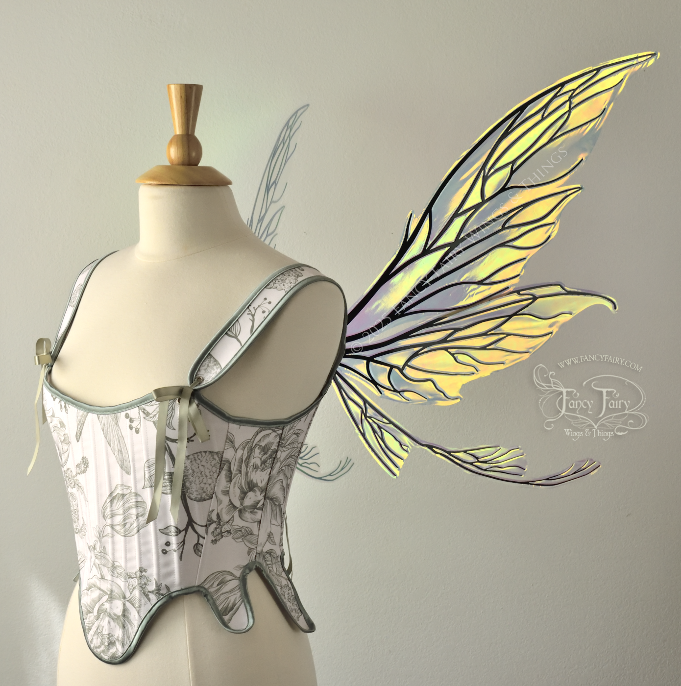 Transparent & iridescent fairy wings reflecting yellow, orange & green with black veins, upper and lower panels are elongated with pointed tips, & curved up ‘tail’ on bottom, worn on a dress form, right side view