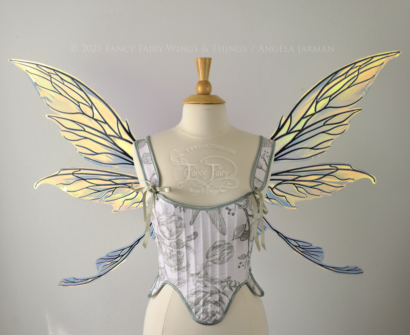 Transparent & iridescent fairy wings reflecting yellow, orange & green with black veins, upper and lower panels are elongated with pointed tips, & curved up ‘tail’ on bottom, worn on a dress form, front view