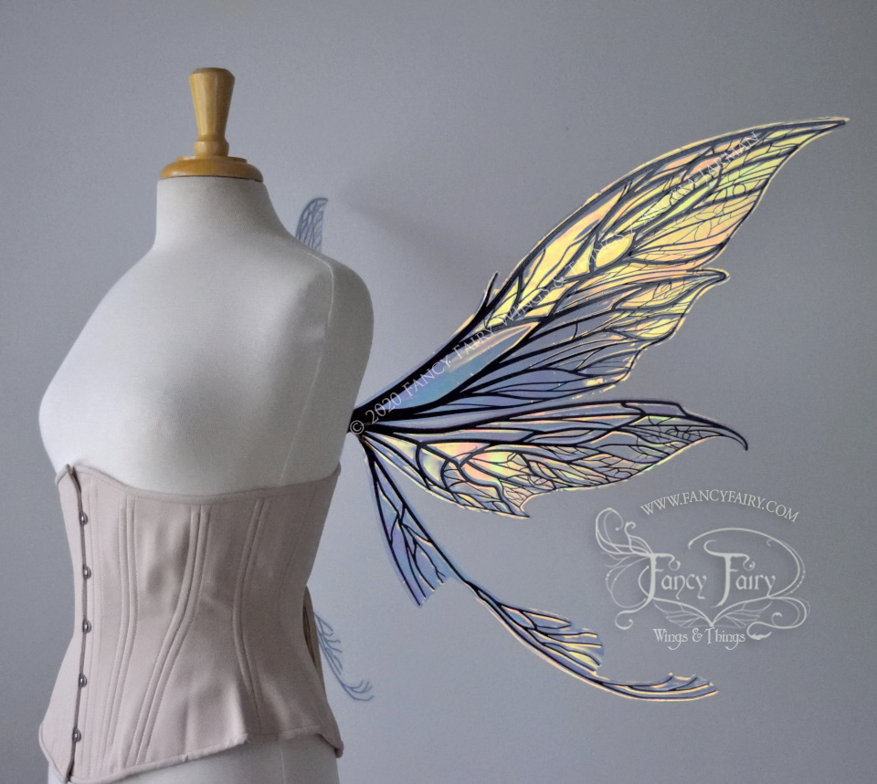 Right side view of an ivory dress form wearing an alabaster underbust corset and large clear iridescent fairy wings with black veins. Upper panels are elongated with pointed tips, curved ‘tail’, lots of thin vein detail