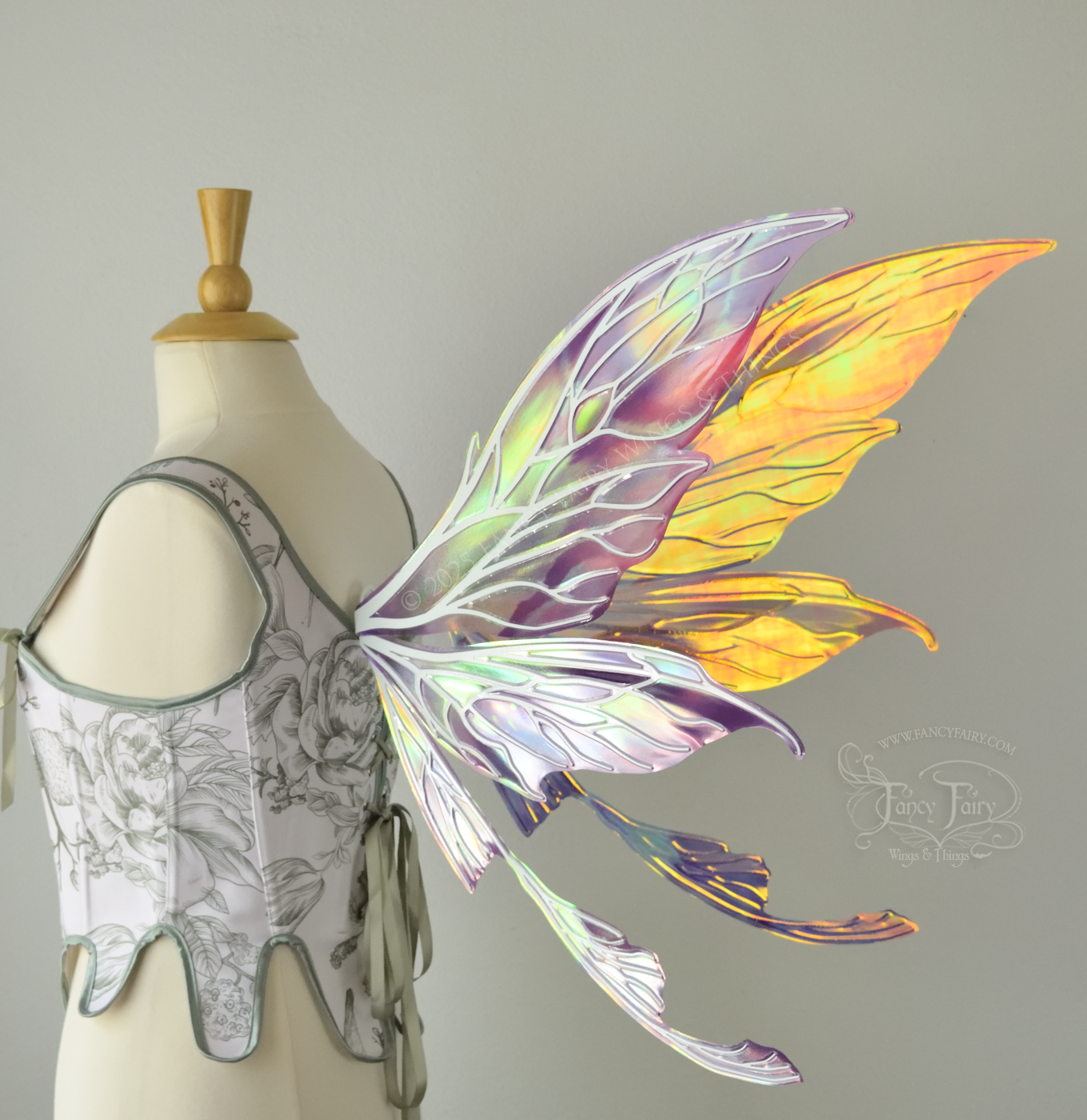 Large painted iridescent fairy wings in berry colors with white veins. Upper panels are elongated with pointed tips, curved ‘tail’, worn on a dress form, back 3/4 view