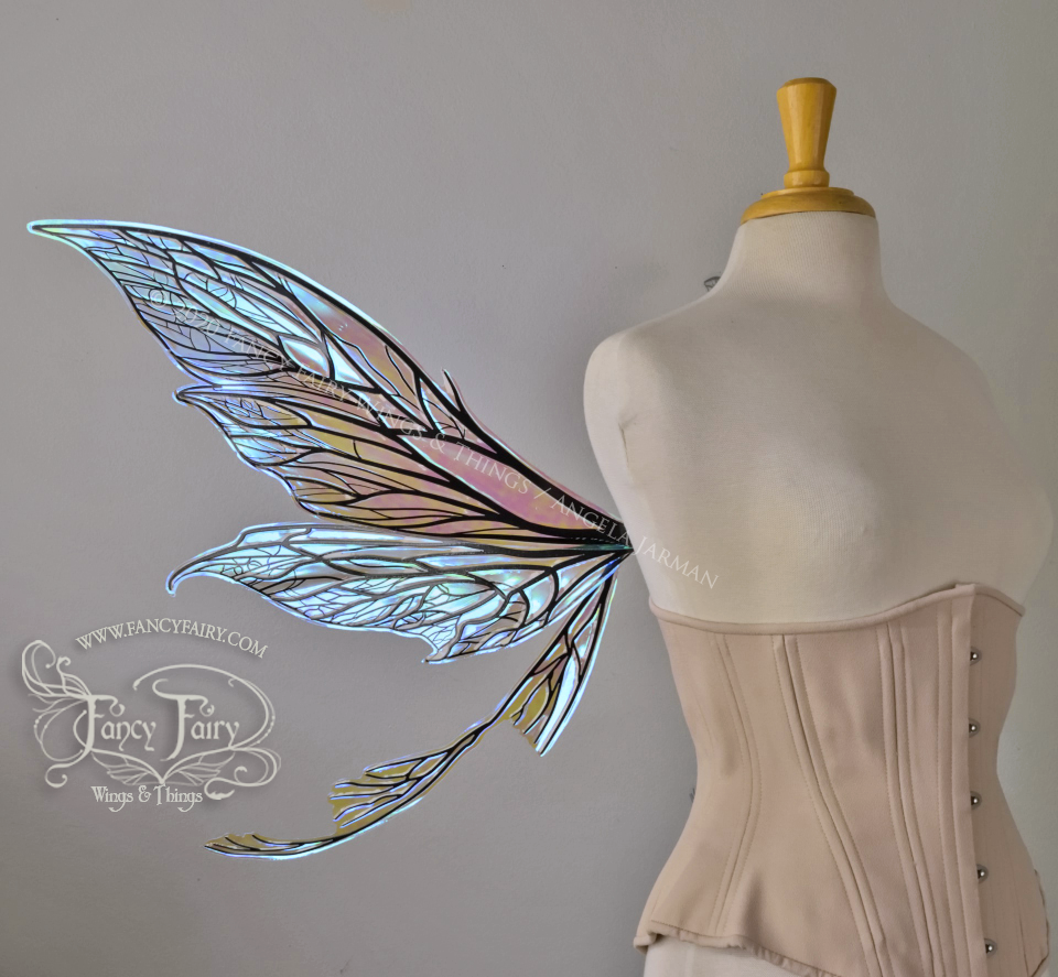 Left side view of an ivory dress form wearing an alabaster underbust corset and large clear blueish iridescent fairy wings with black veins. Upper panels are elongated with pointed tips, curved ‘tail’, lots of thin vein detail
