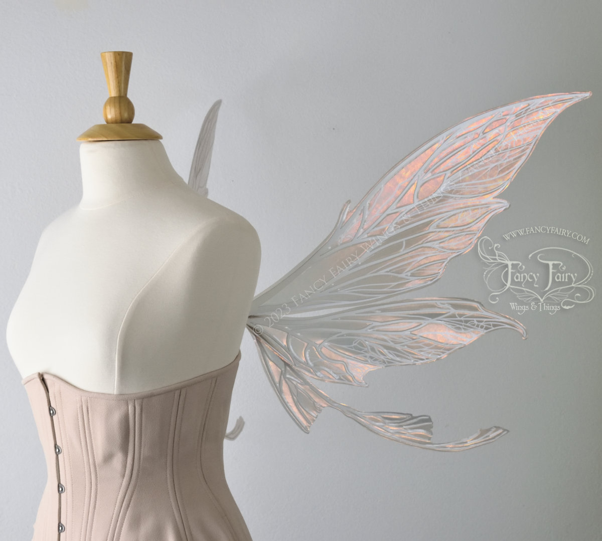 Rt Side view of a dress form wearing an underbust corset & large Rose Gold iridescent fairy wings with tails & lots of detailed white veins.