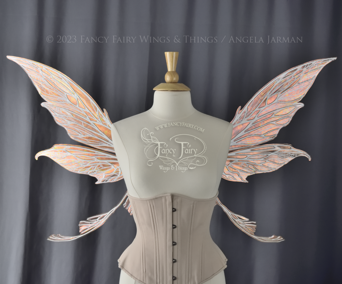 Front view of a dress form wearing an underbust corset and large Rose Gold iridescent fairy wings with tails & lots of detailed white veins.