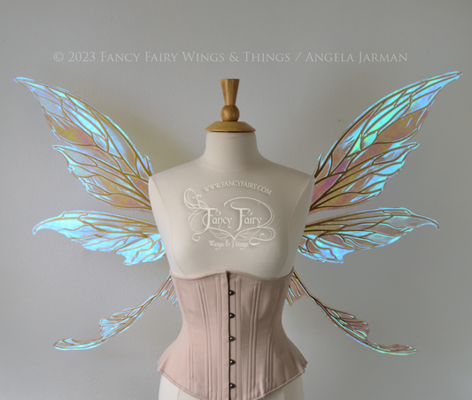 Front view of a dress form wearing an underbust corset & large blue iridescent fairy wings with gold veins. Upper panels are elongated with pointed tips, curved ‘tail’ 
