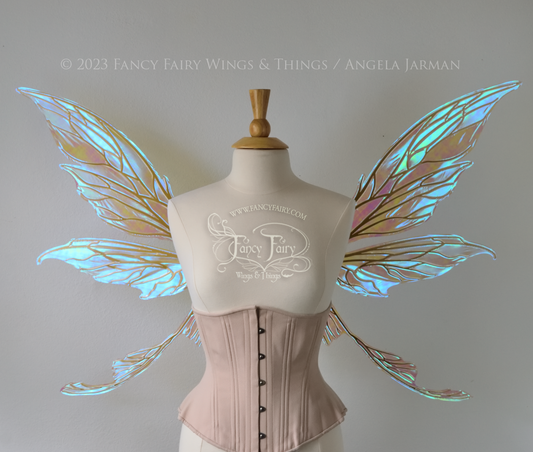 Front view of a dress form wearing an underbust corset & large blue iridescent fairy wings with gold veins. Upper panels are elongated with pointed tips, curved ‘tail’