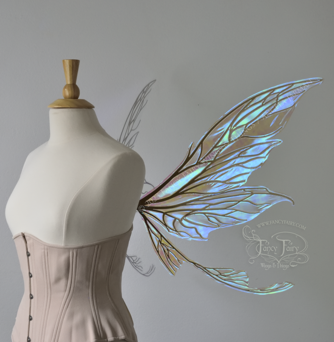 Side view of a dress form wearing an underbust corset & large blue iridescent fairy wings with gold veins. Upper panels are elongated with pointed tips, curved ‘tail’ 