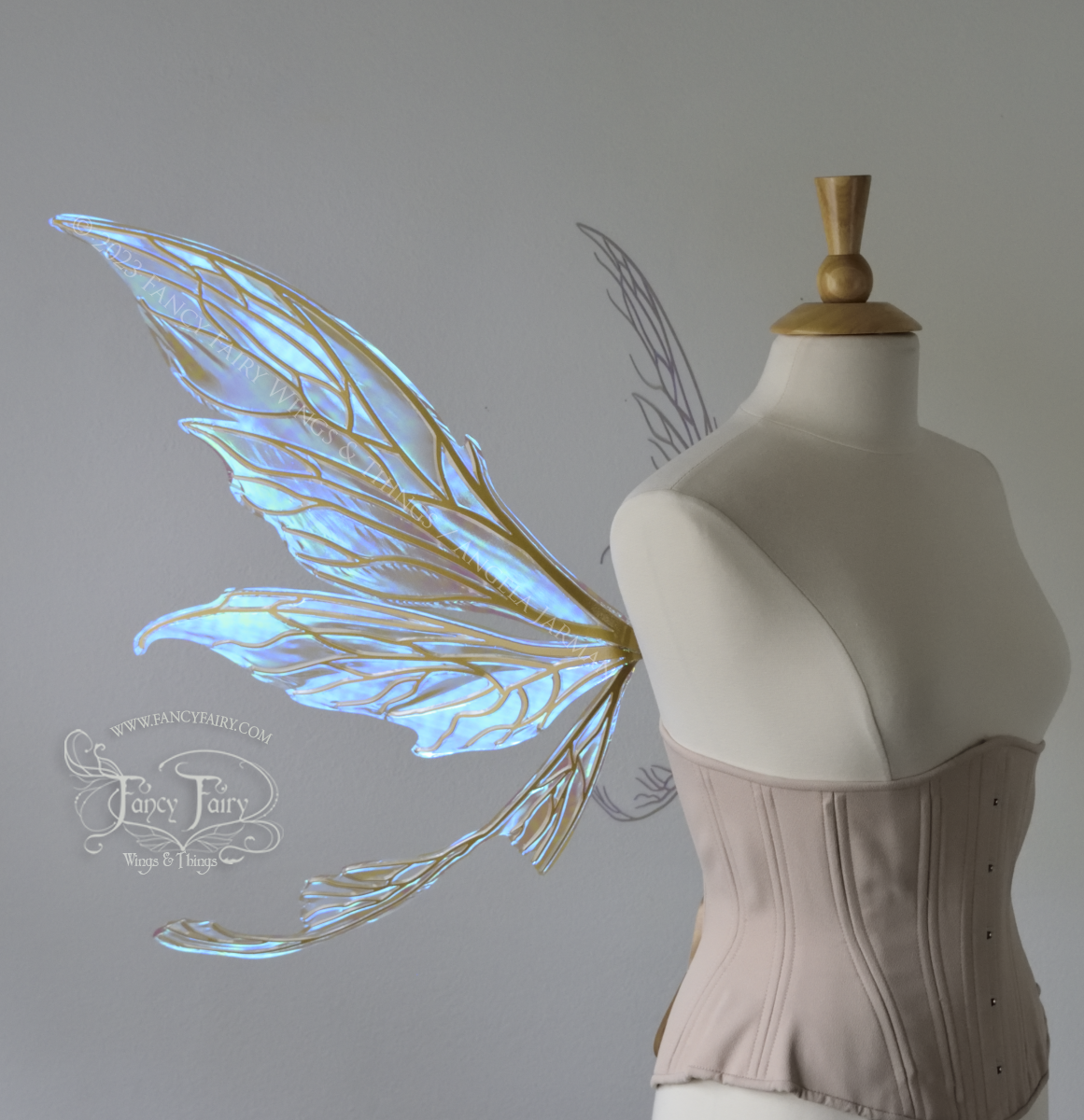 Right side view of a dress form wearing an underbust corset & large blue iridescent fairy wings with gold veins. Upper panels are elongated with pointed tips, curved ‘tail’ 