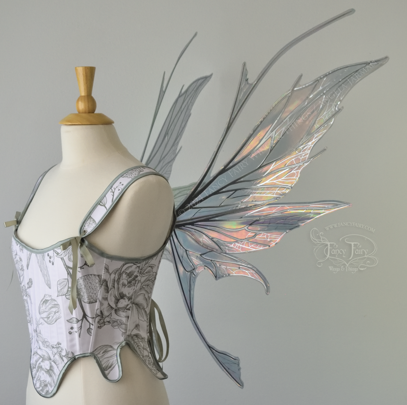 Right side view of a dress form wearing a white & green corset and large oil slick colored iridescent fairy wings with antennae on top, 3 panels each side, upper panels come to a point, bottom panels have tails, spikey, detailed silver veins