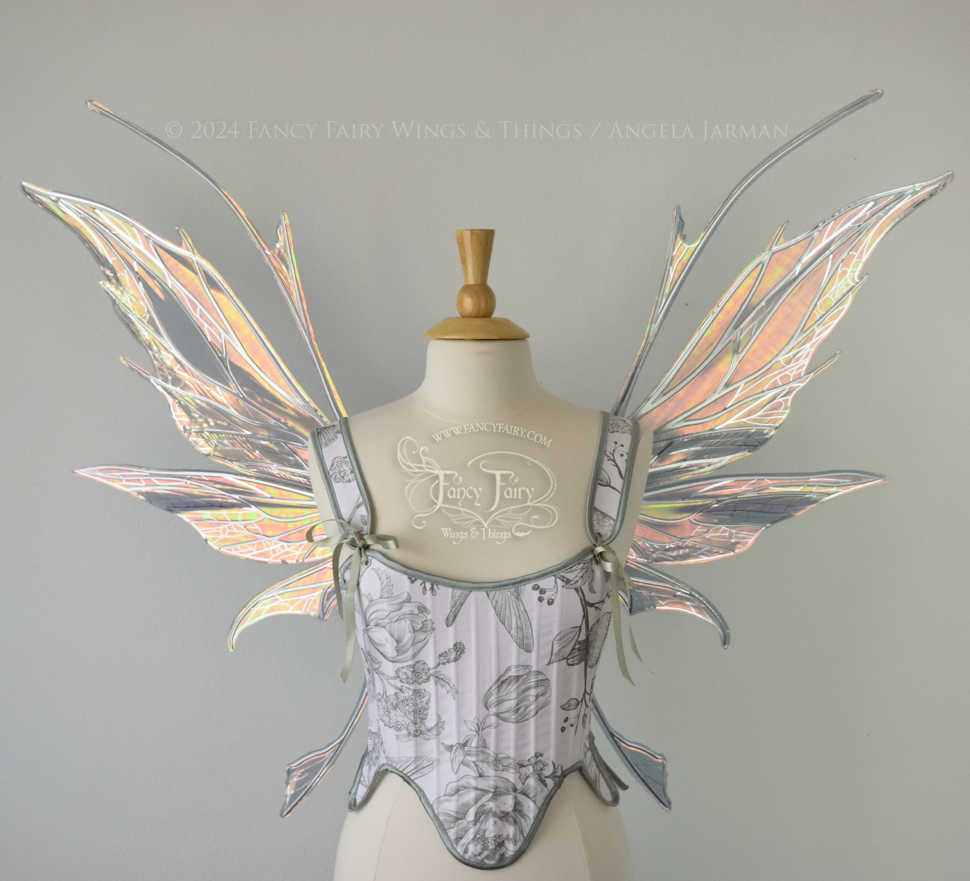 Front view of a dress form wearing a white & green corset and large oil slick colored iridescent fairy wings with antennae on top, 3 panels each side, upper panels come to a point, bottom panels have tails, spikey, detailed silver veins