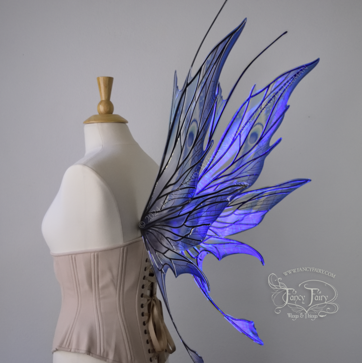 Back 3/4 view of large spikey blue painted iridescent fairy wings with antennae along the top & black detailed veins, displayed on dress form. 