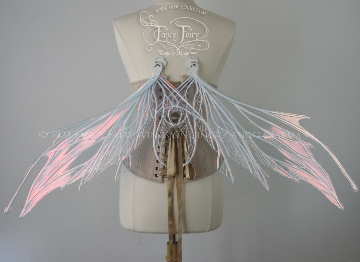 Back view of an ivory dress form wearing an alabaster underbust corset and large pink iridescent fairy wings with antennae in the downward resting position. Upper panels come to a point, bottom panels have tails. Spikey, detailed white veins, plain white / grey background