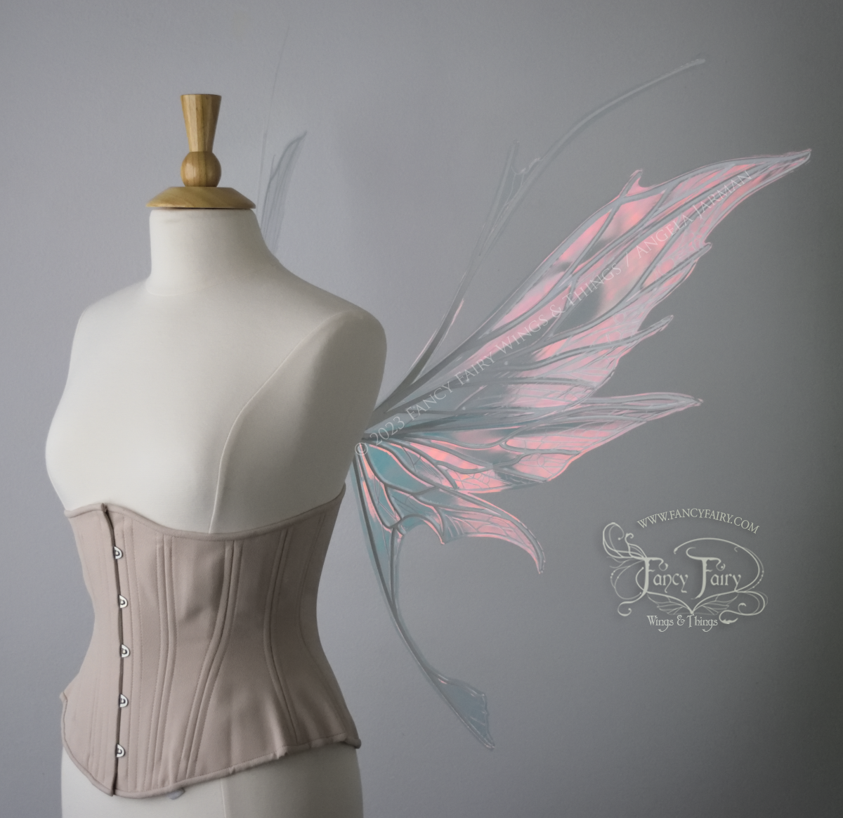 Right side view of an ivory dress form wearing an alabaster underbust corset and large pink iridescent fairy wings with antennae on top. Upper panels come to a point, bottom panels have tails. Spikey, detailed white veins, plain white / grey background