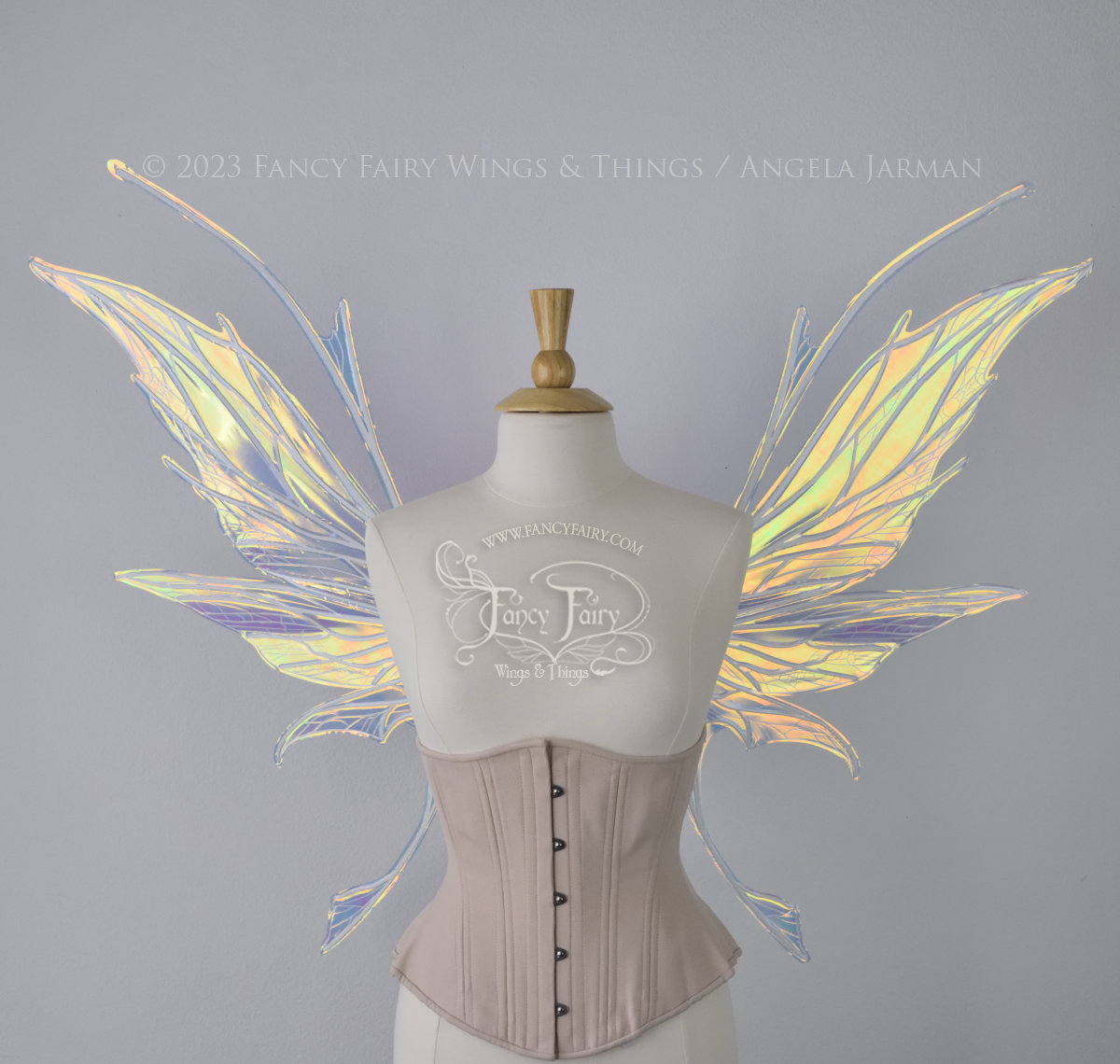 Front view of an ivory dress form wearing an alabaster underbust corset and large multicolor iridescent fairy wings featuring antennae along the top. Upper panels come to a point as do the middle panels, bottom panels have tails. Spikey, detailed white veins. The background is white / light grey