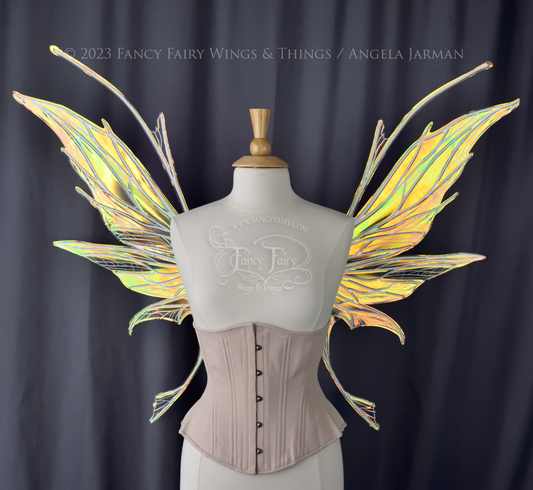 Front view of an ivory dress form wearing an alabaster underbust corset and large multicolor iridescent fairy wings featuring antennae along the top. Upper panels come to a point as do the middle panels, bottom panels have tails. Spikey, detailed white veins. The background is dark grey