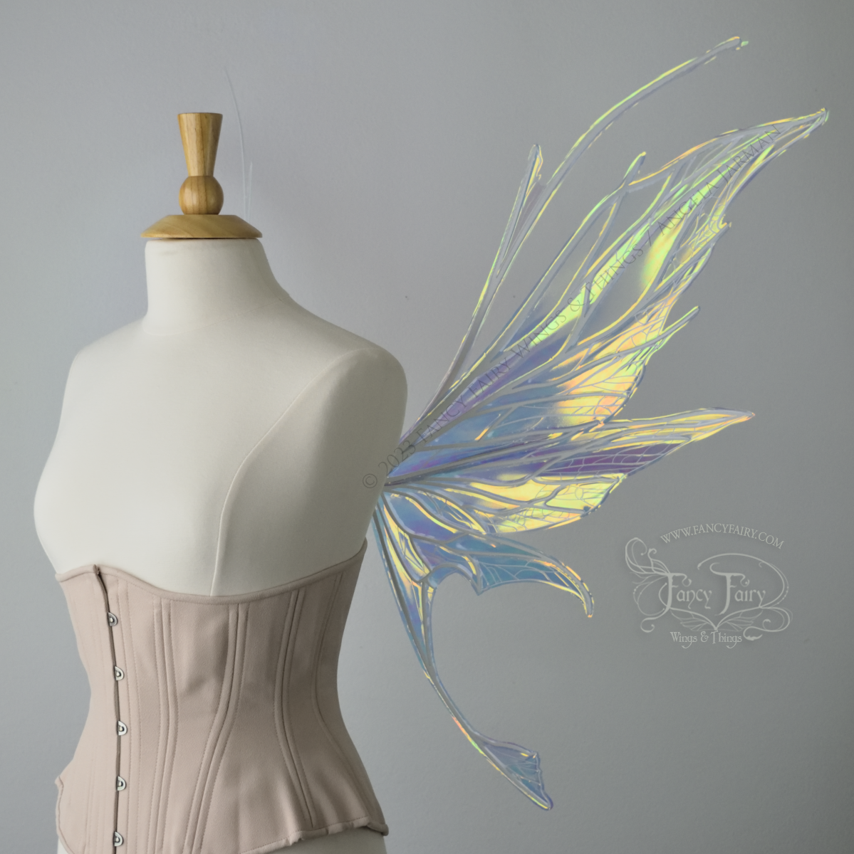 Right side view of an ivory dress form wearing an alabaster underbust corset and large multicolor iridescent fairy wings featuring antennae along the top. Upper panels come to a point as do the middle panels, bottom panels have tails. Spikey, detailed white veins. The background is white / light grey