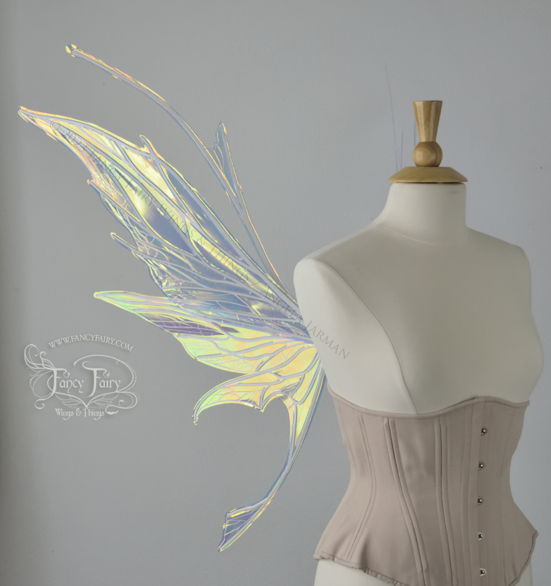 Left side view of an ivory dress form wearing an alabaster underbust corset and large multicolor iridescent fairy wings featuring antennae along the top. Upper panels come to a point as do the middle panels, bottom panels have tails. Spikey, detailed white veins. The background is white / light grey