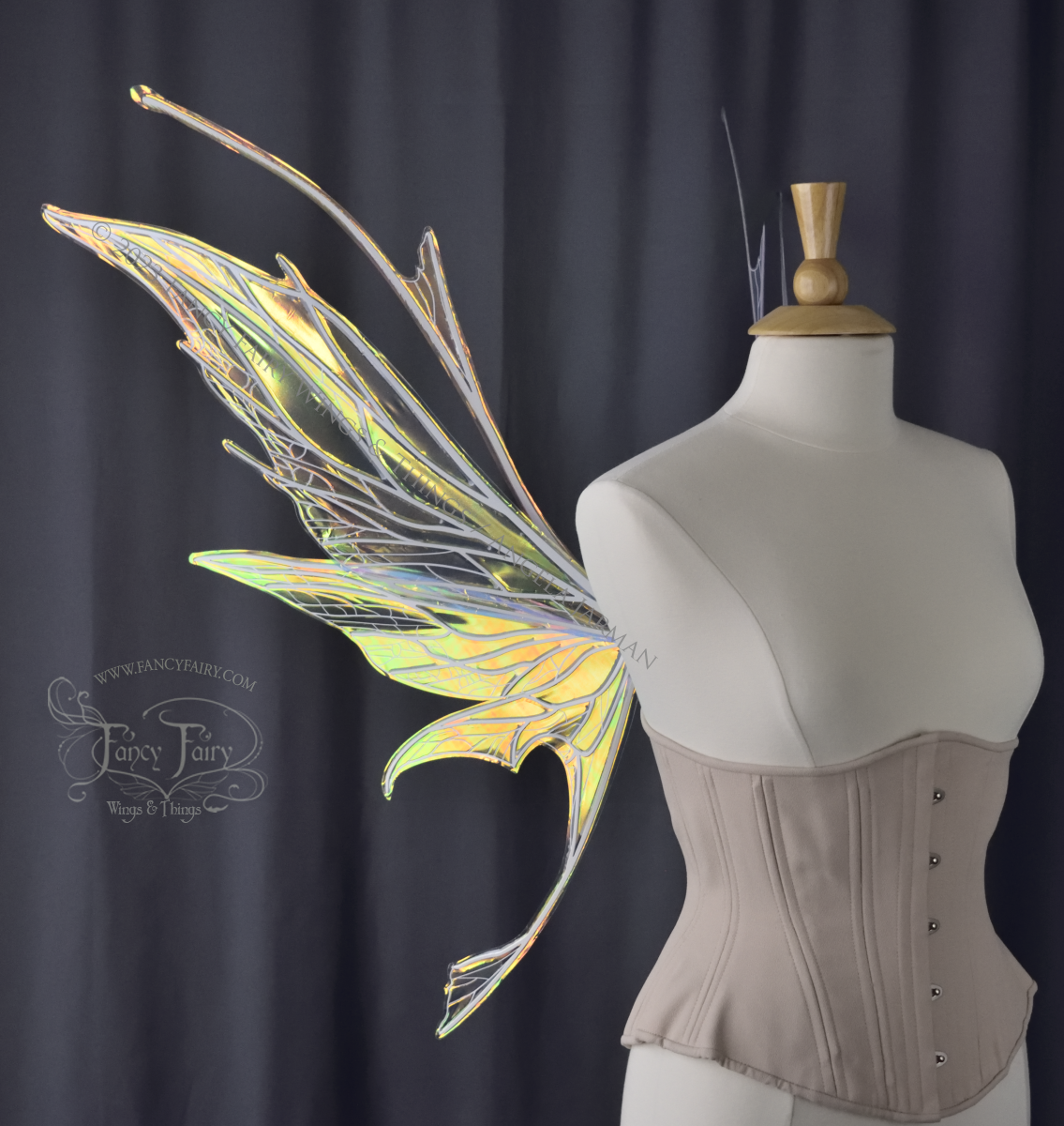 Left side view of an ivory dress form wearing an alabaster underbust corset and large multicolor iridescent fairy wings featuring antennae along the top. Upper panels come to a point as do the middle panels, bottom panels have tails. Spikey, detailed white veins. The background is dark grey