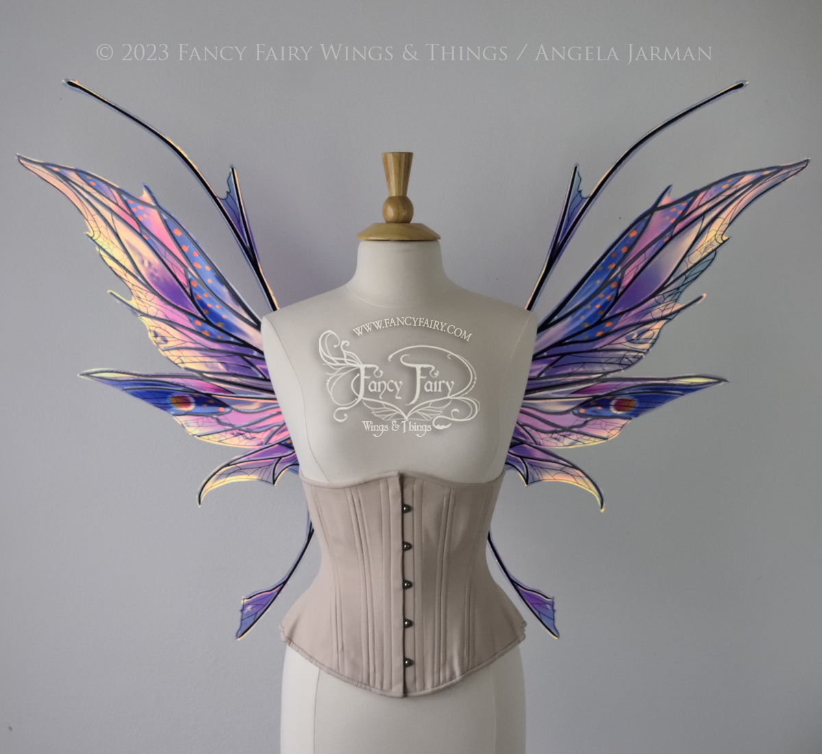 Front view of a dress form wearing an underbust corset & large blue / lavender / red painted iridescent fairy wings with antennae, black veins, spikey shapes