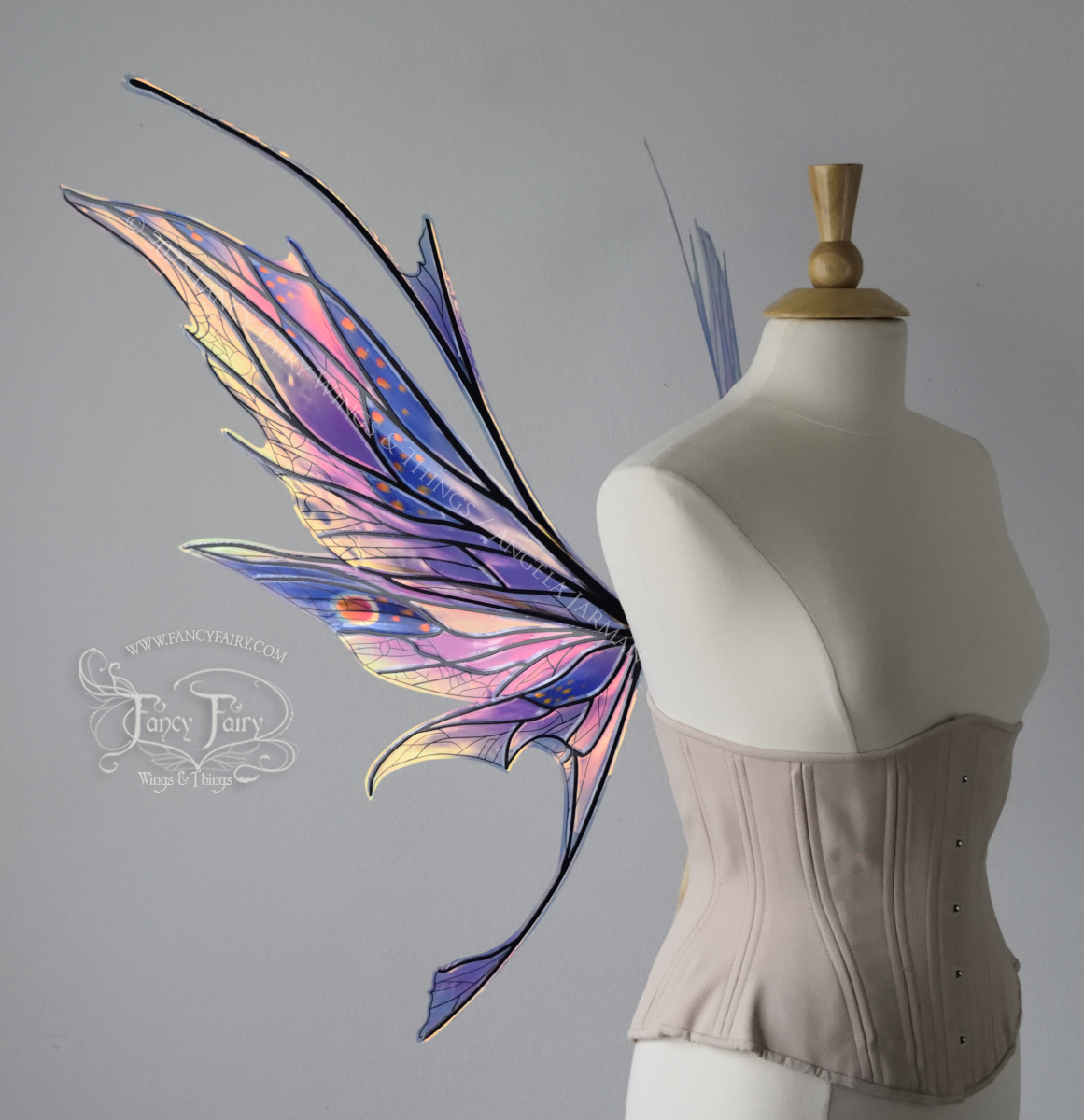 Left side view of a dress form wearing an underbust corset & large blue / lavender / red painted iridescent fairy wings with antennae, black veins, spikey shapes