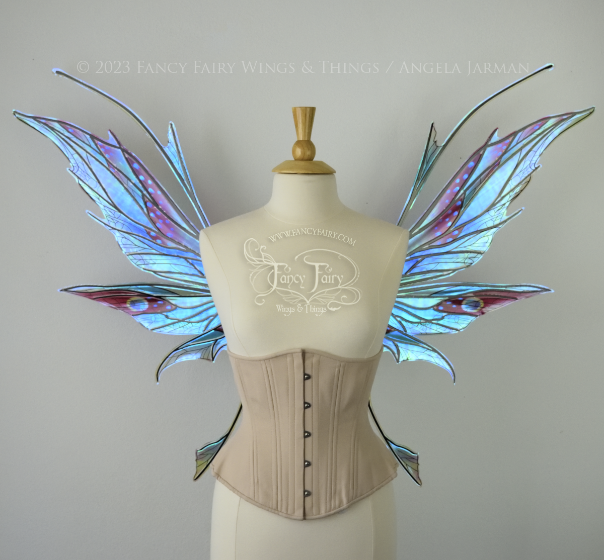 Front view of a dress form wearing an underbust corset & large blue / burgundy / green painted iridescent fairy wings with antennae, black veins, spikey shapes