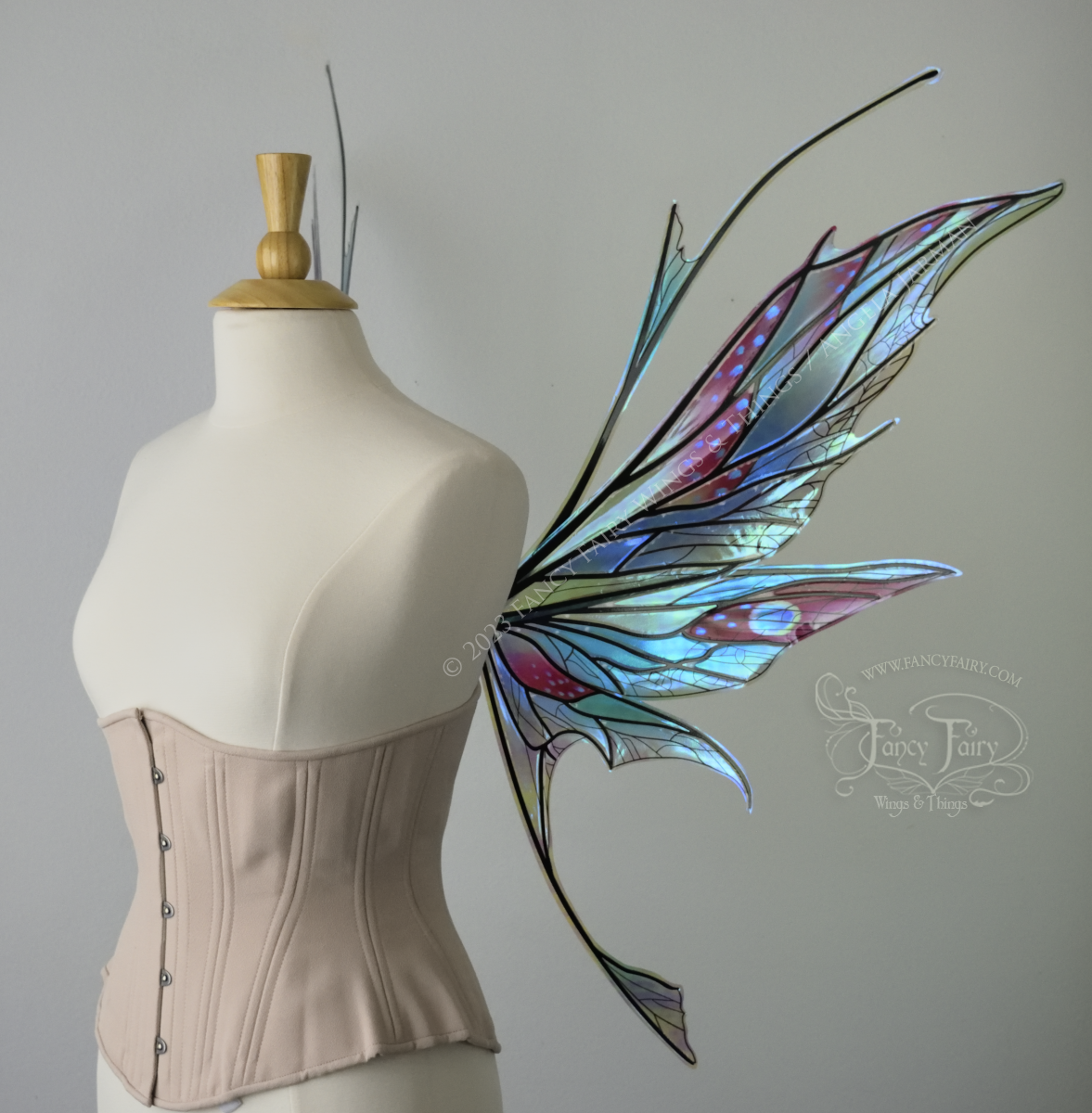 Right side view of a dress form wearing an underbust corset & large blue / burgundy / green painted iridescent fairy wings with antennae, black veins, spikey shapes