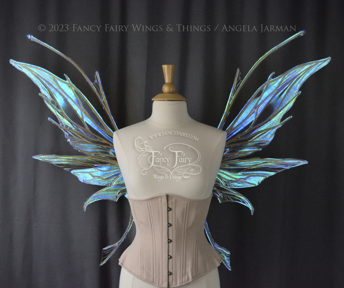 Front view of a dress form wearing an underbust corset & large blue/green iridescent fairy wings with antennae, gold veins, spikey shapes, grey background