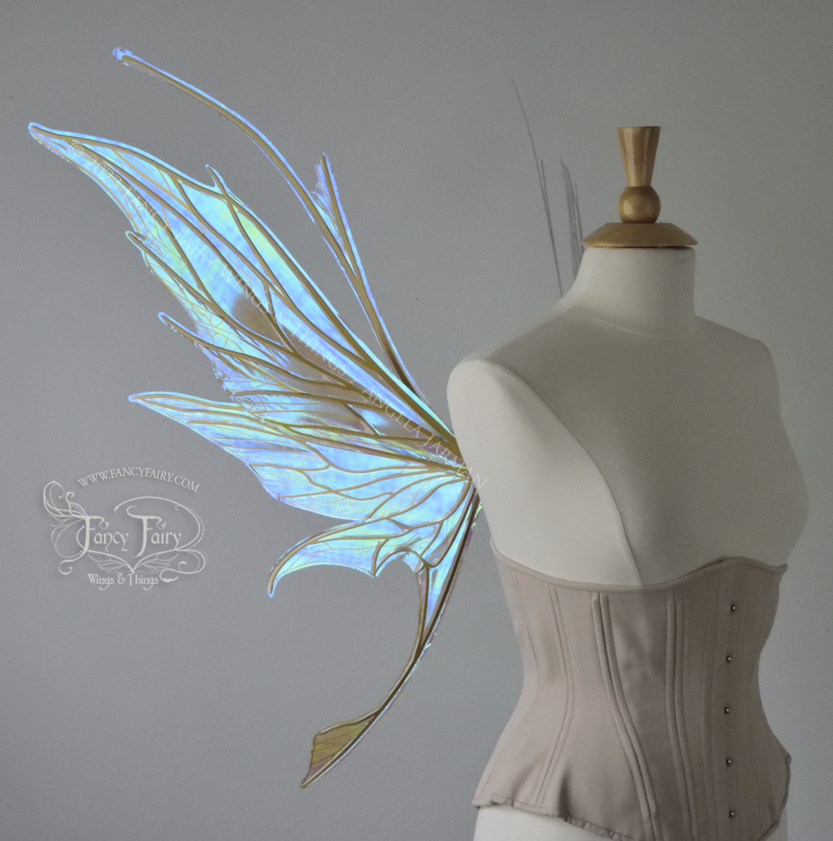 Left side view of a dress form wearing an underbust corset & large blue/green iridescent fairy wings with antennae, gold veins, spikey shapes