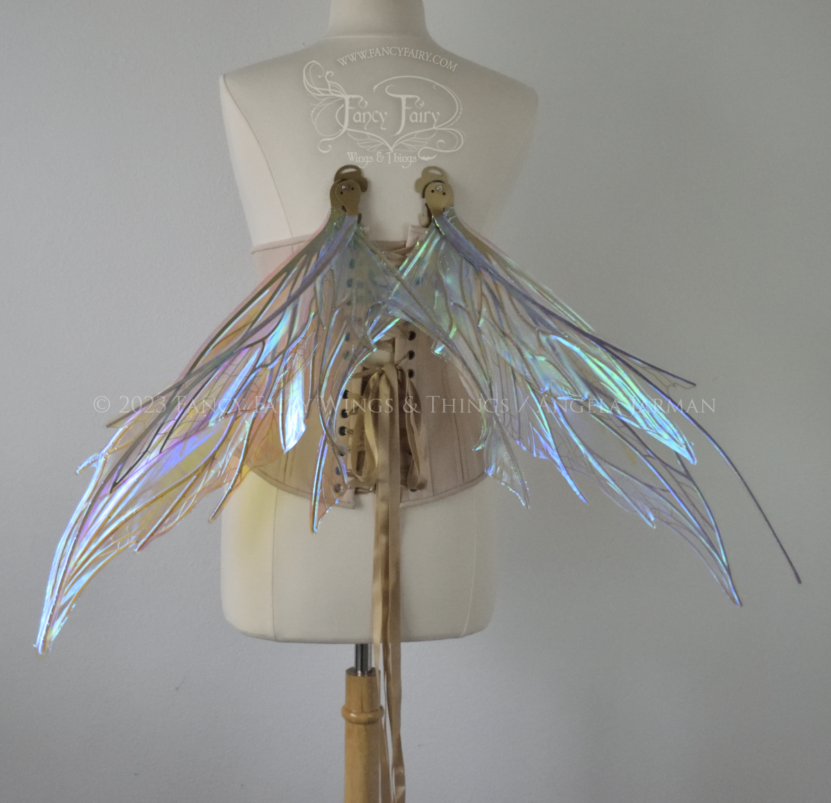 Back view of a dress form wearing an underbust corset & large blue/green iridescent fairy wings with antennae, gold veins, spikey shapes, in resting position