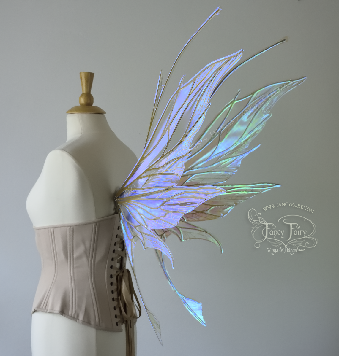 Back 3/4 view of a dress form wearing an underbust corset & large blue/green iridescent fairy wings with antennae, gold veins, spikey shapes