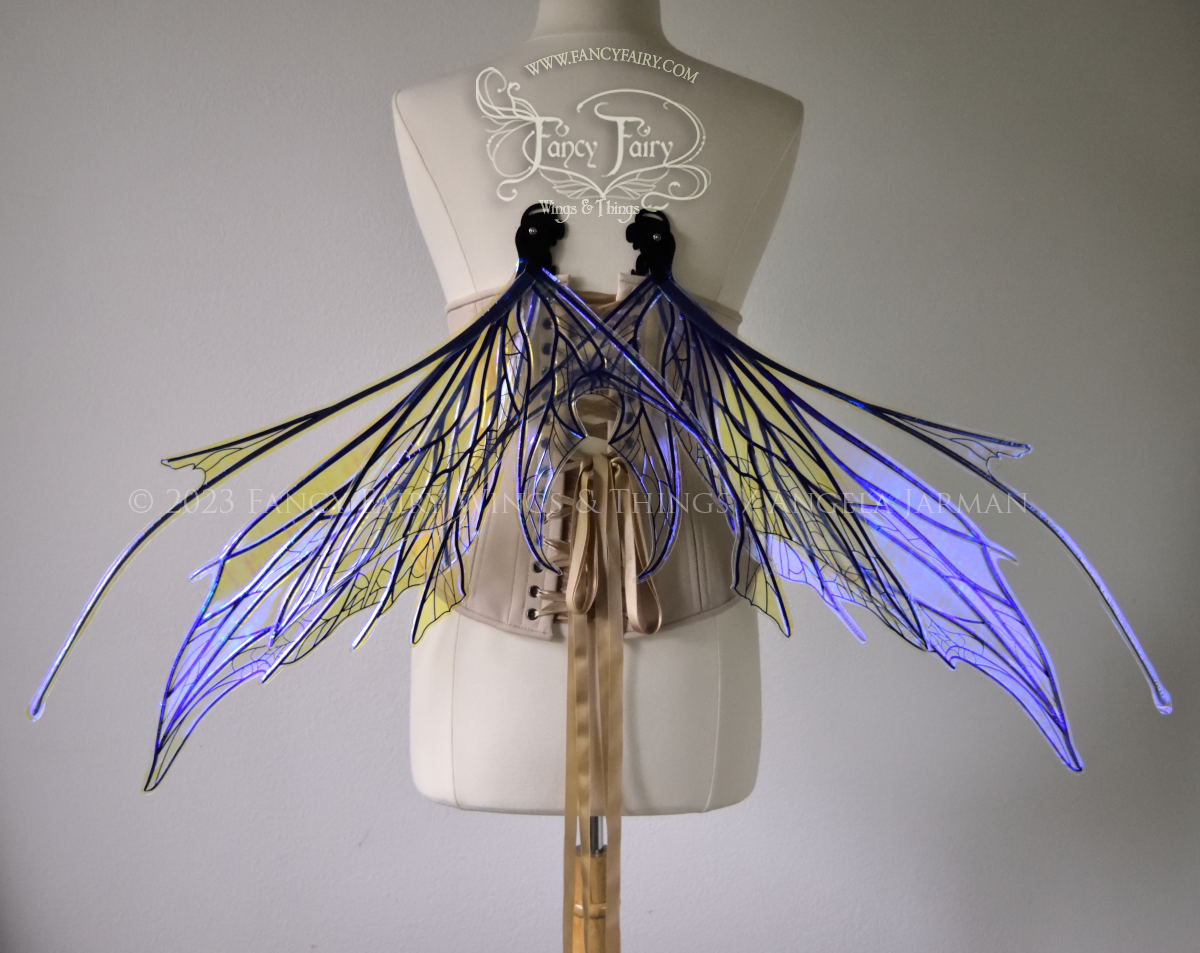 Back view of a dress form wearing an underbust corset & large violet iridescent fairy wings with antennae, black veins, spikey shapes in resting position
