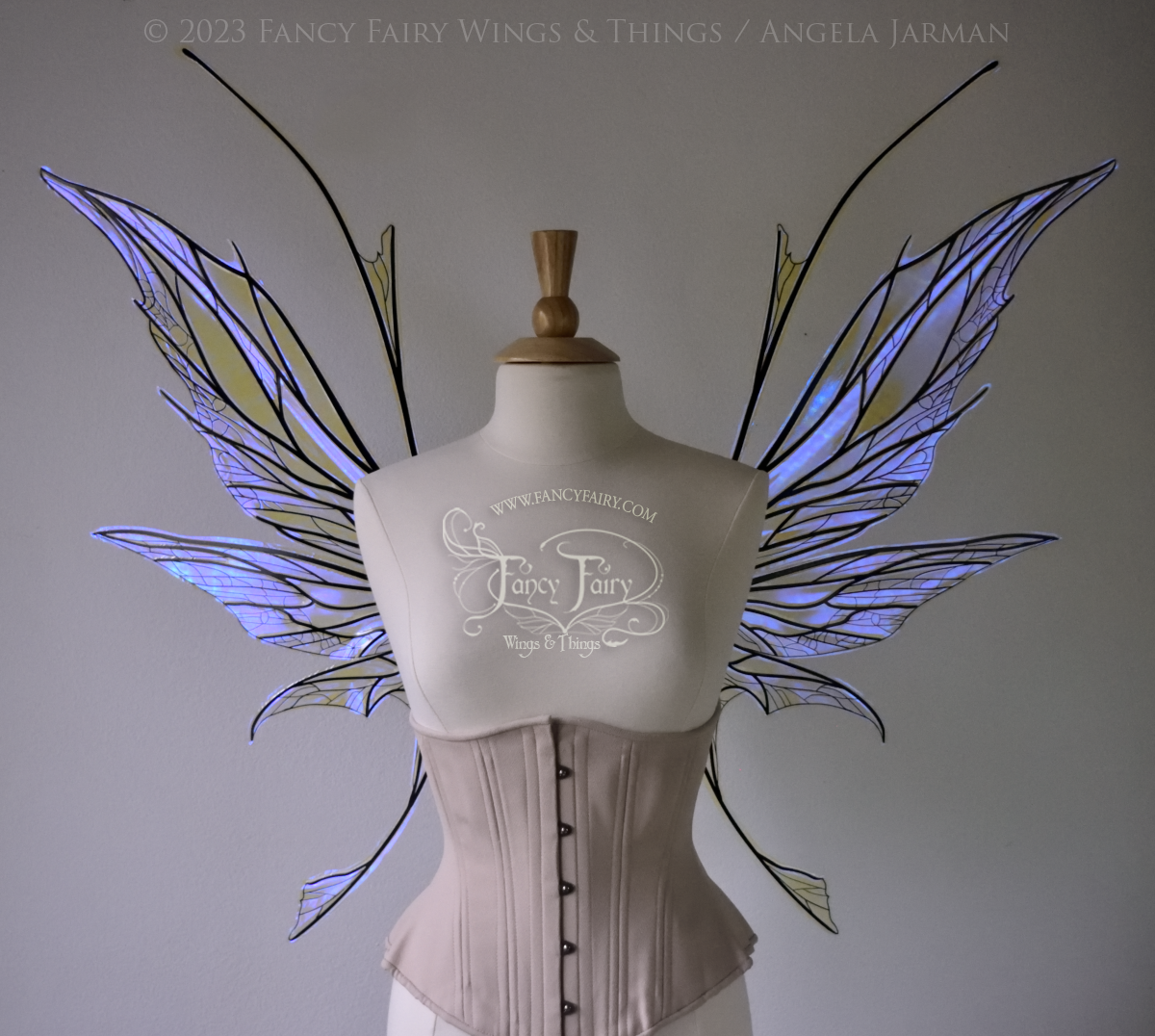 Front view of a dress form wearing an underbust corset & large violet iridescent fairy wings with antennae, black veins, spikey shapes