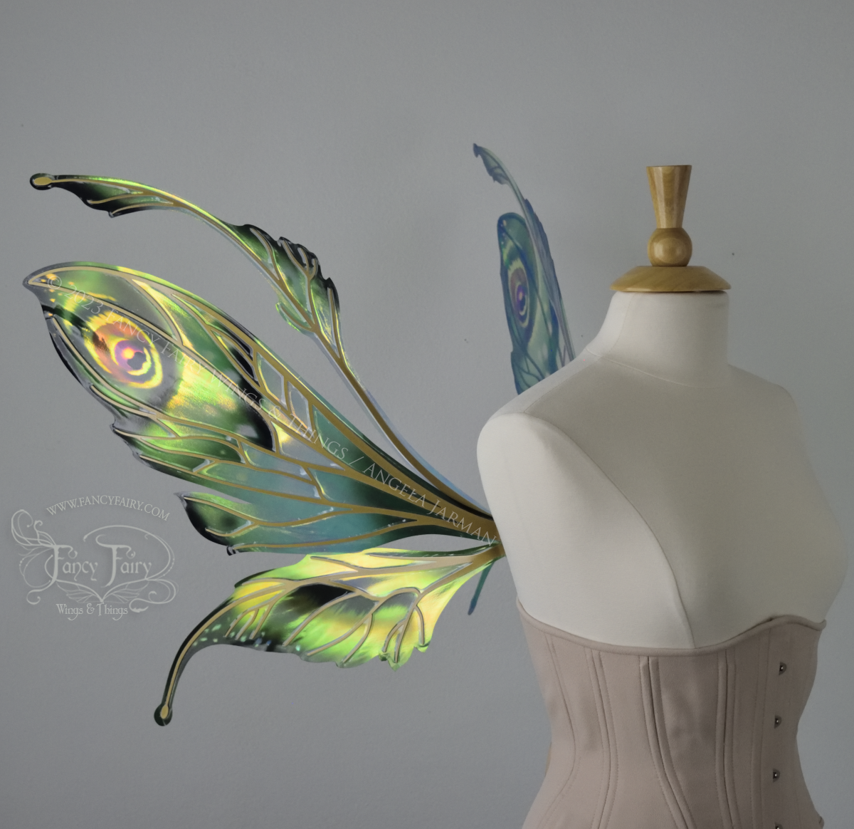 Left side view of a dress form wearing an underbust corset & large iridescent fairy wings with green & gold color pattern