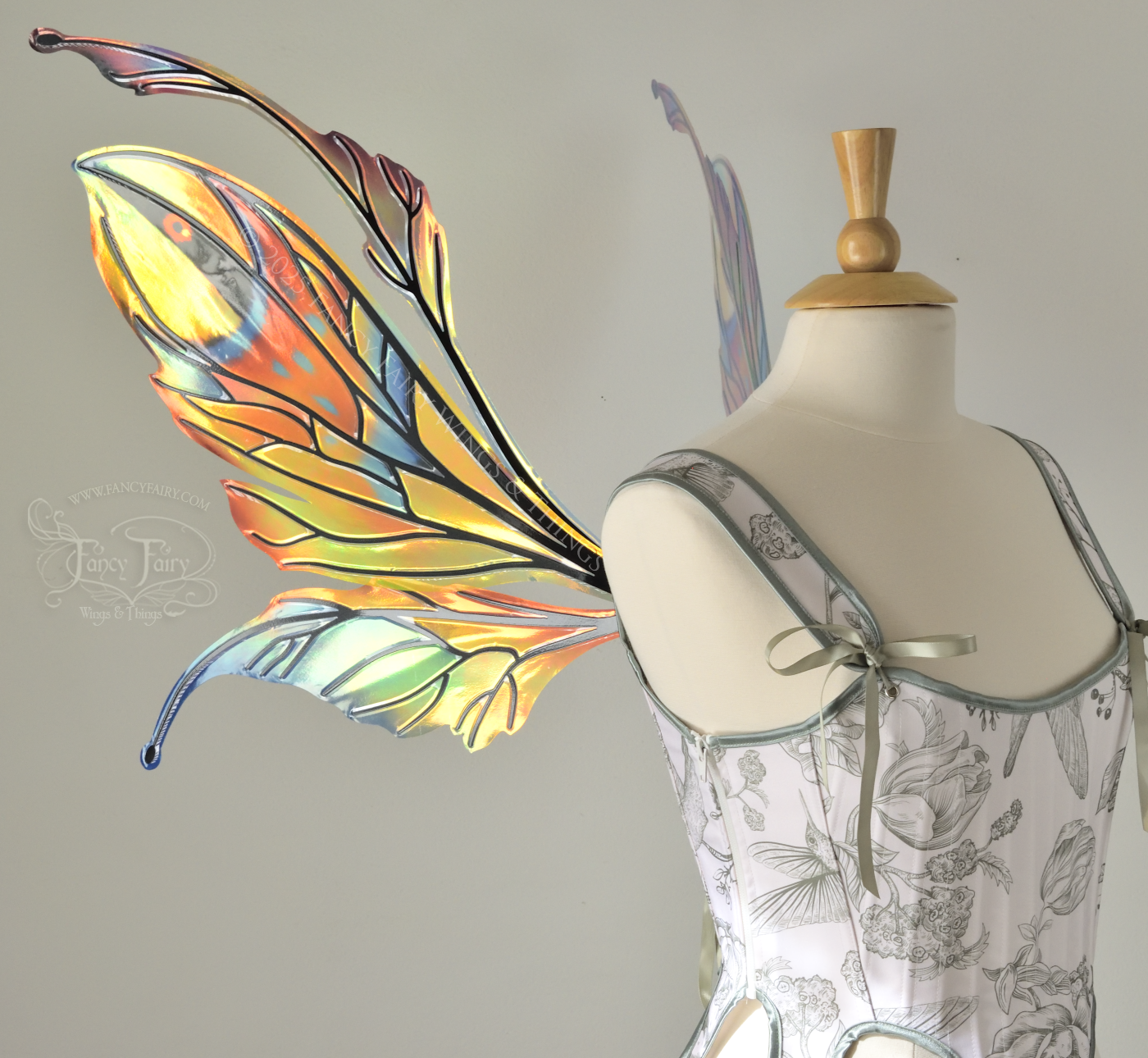 Brightly colored iridescent fairy wings in oranges, yellows, teals and blues with black veins, antennae along the top, worn on a dress form, left side view