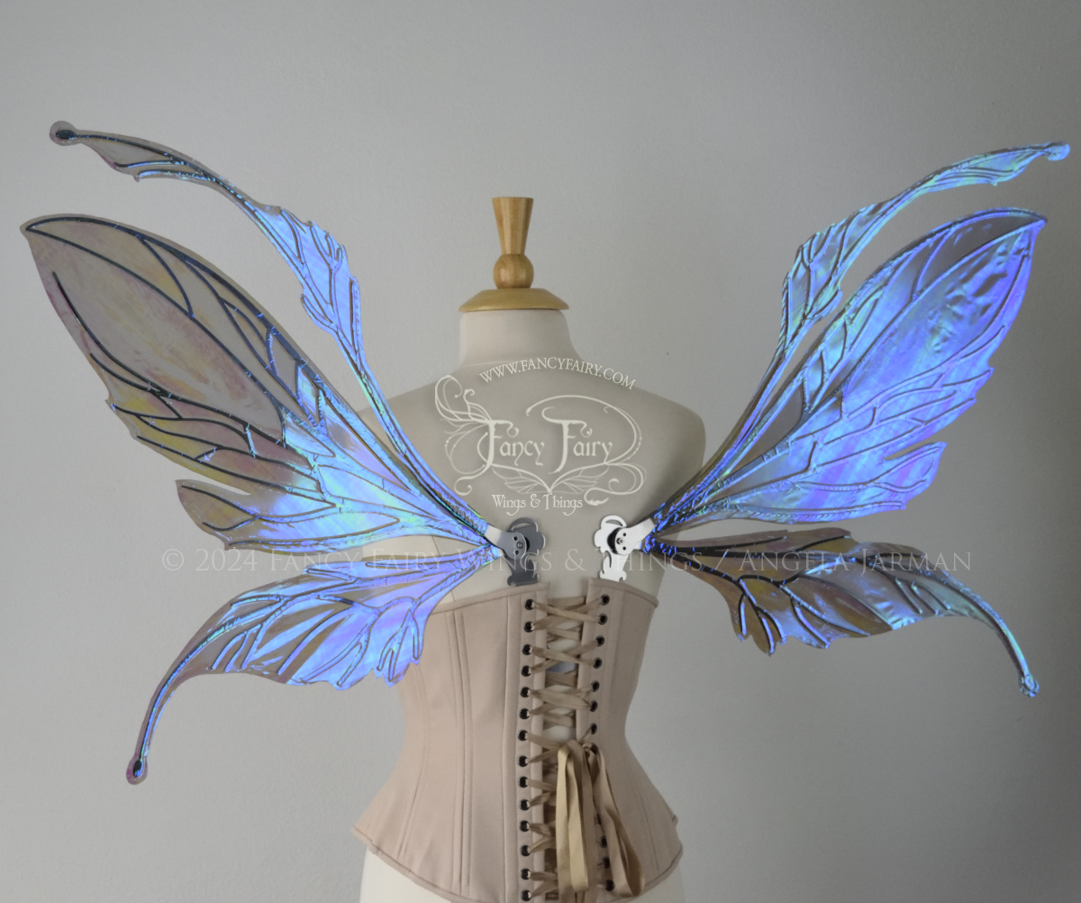 Back view of a dress form wearing an underbust corset & large iridescent purple fairy wings with antennae. The upper panels are elongated with semi-pointed tips, the lower panels are smaller with downward curved tips, veins are silver.