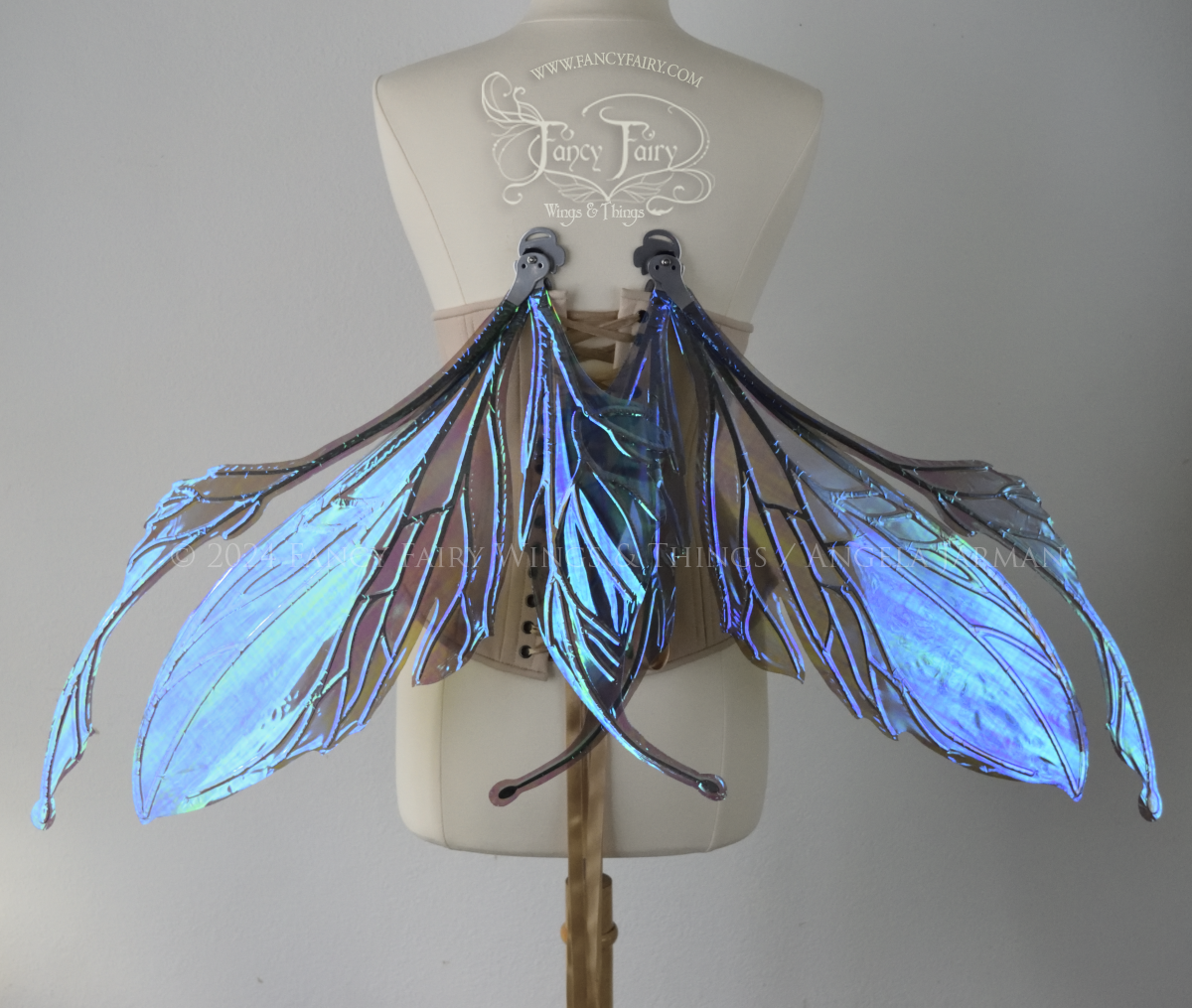 Back view of a dress form wearing an underbust corset & large iridescent purple fairy wings with antennae. The upper panels are elongated with semi-pointed tips, the lower panels are smaller with downward curved tips, veins are silver. Wings are in resting position