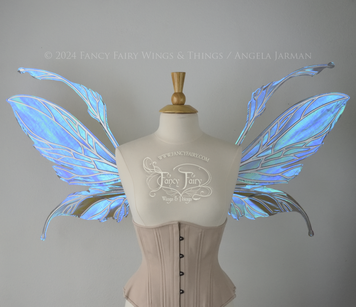 Front view of a dress form wearing an underbust corset & large iridescent purple fairy wings with antennae. The upper panels are elongated with semi-pointed tips, the lower panels are smaller with downward curved tips, veins are silver.