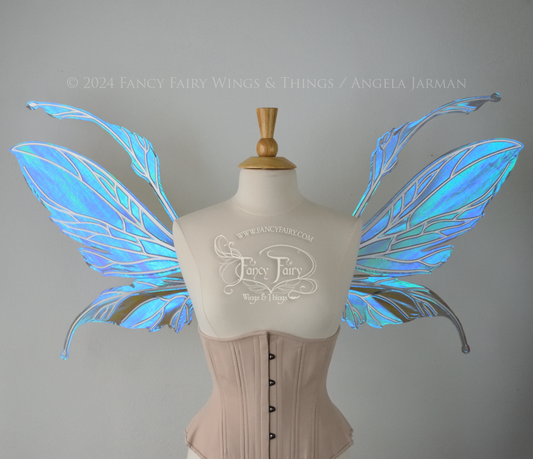 Front view of a dress form wearing an underbust corset & large iridescent purple fairy wings with antennae. The upper panels are elongated with semi-pointed tips, the lower panels are smaller with downward curved tips, veins are silver.