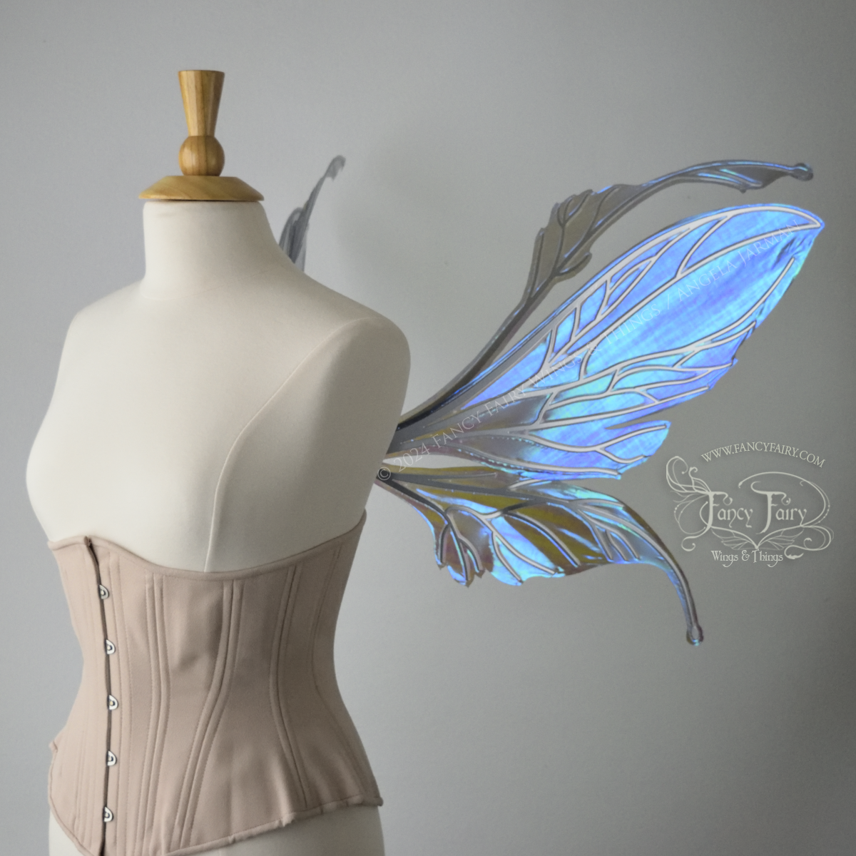 Right side view of a dress form wearing an underbust corset & large iridescent purple fairy wings with antennae. The upper panels are elongated with semi-pointed tips, the lower panels are smaller with downward curved tips, veins are silver.