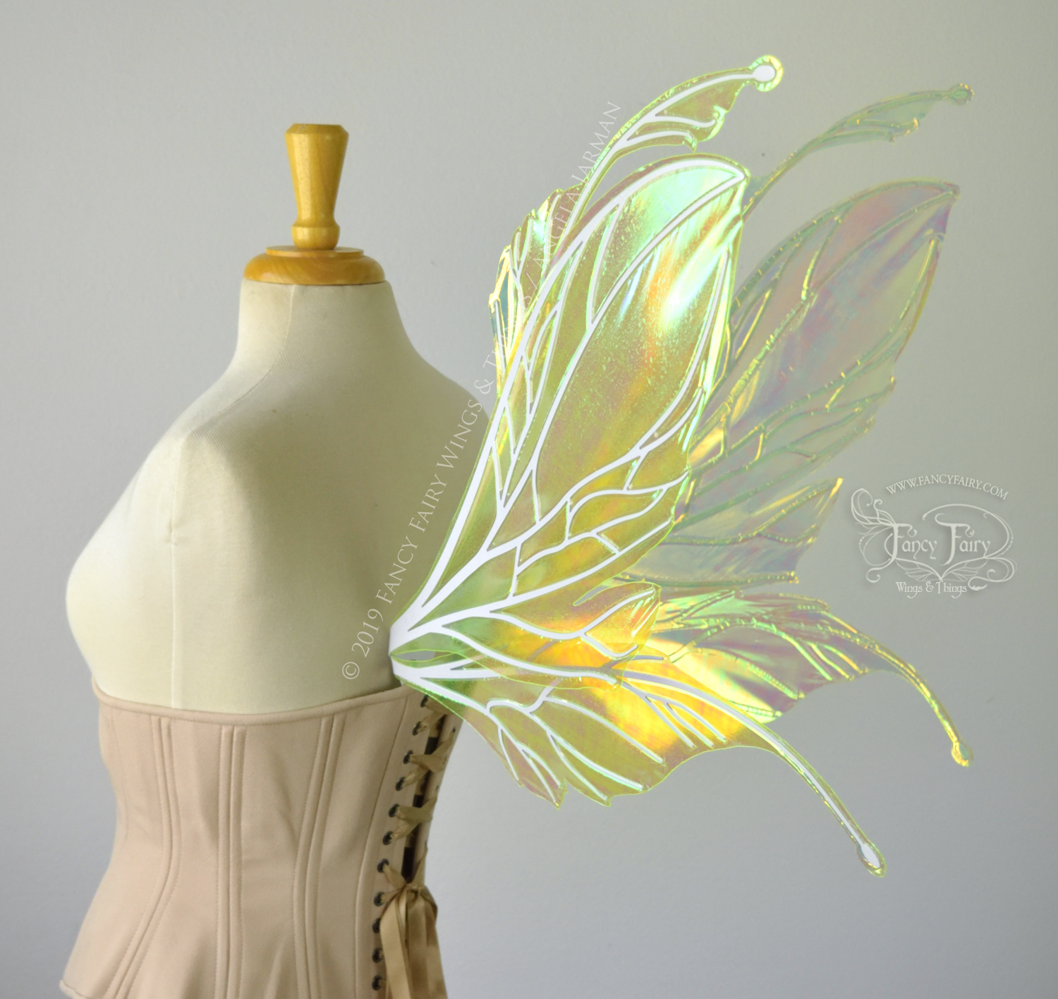 Back 3/4 view of a dress form wearing an underbust corset and large fairy wings featuring antennae along the top. The upper panels are elongated with semi-pointed tips, the lower panels are smaller with slender tips that curve downward. They are neon yellow iridescent and the veins are white. The background is plain white and my logo and copyright notice are visible.