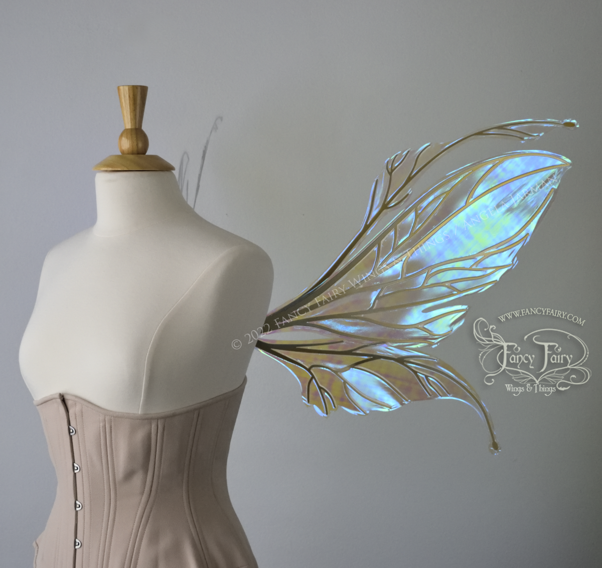 Right side view of an ivory dress form wearing an alabaster underbust corset and large fairy wings featuring antennae along the top. The upper panels are elongated with semi-pointed tips, the lower panels are smaller with slender tips that curve downward. They are transparent iridescent with a mostly blue shine with some green and the veins are metallic gold. The background is plain white and my logo and copyright notice are visible.