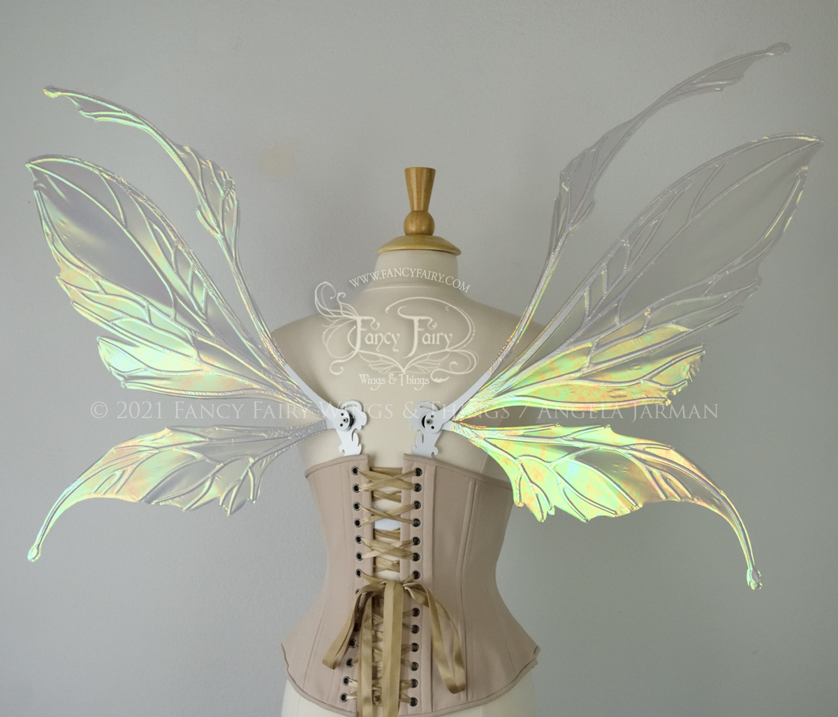 Back view of an ivory dress form wearing an alabaster underbust corset and large fairy wings featuring antennae along the top. The upper panels are elongated with semi-pointed tips, the lower panels are smaller with slender tips that curve downward. They are patina green iridescent with a green & orange shine and the veins are white. The background is plain white and my logo and copyright notice are visible.