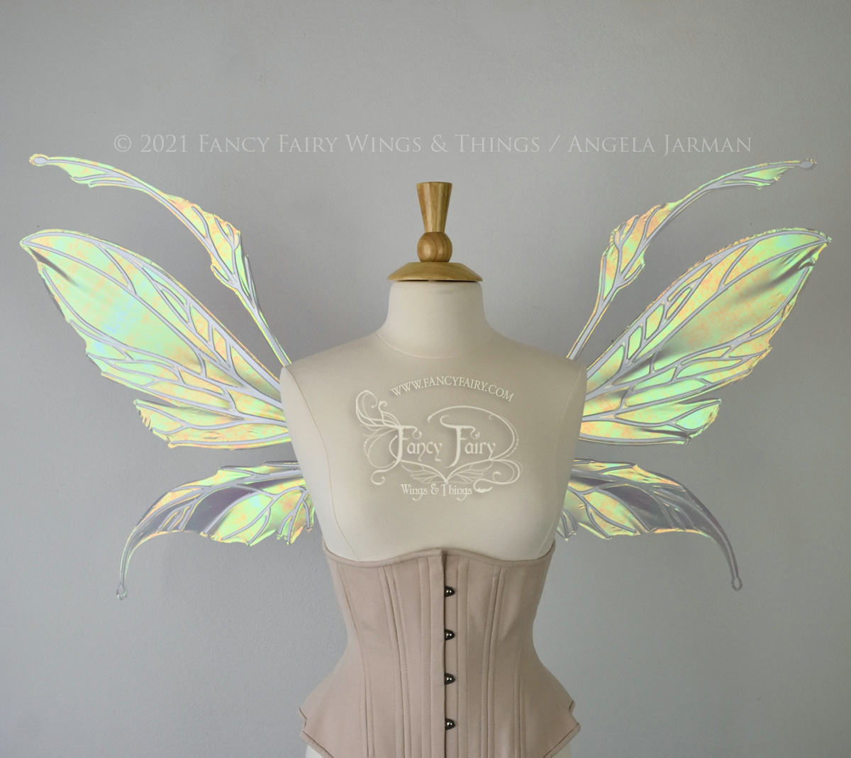 Front view of an ivory dress form wearing an alabaster underbust corset and large fairy wings featuring antennae along the top. The upper panels are elongated with semi-pointed tips, the lower panels are smaller with slender tips that curve downward. They are patina green iridescent with a green & orange shine and the veins are white. The background is plain white and my logo and copyright notice are visible.