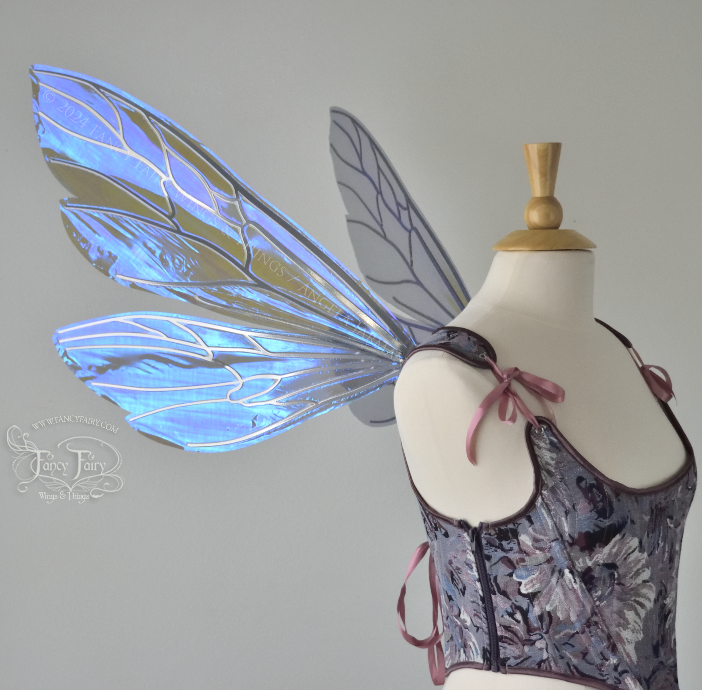 Large fairy wings similar in shape to wasp wings, are iridescent violet / blue with silver veins, left side view