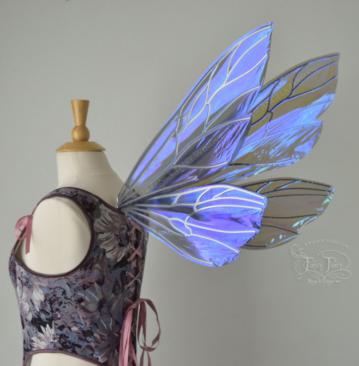 Large fairy wings similar in shape to wasp wings, are iridescent violet / blue with silver veins, back 3/4 view