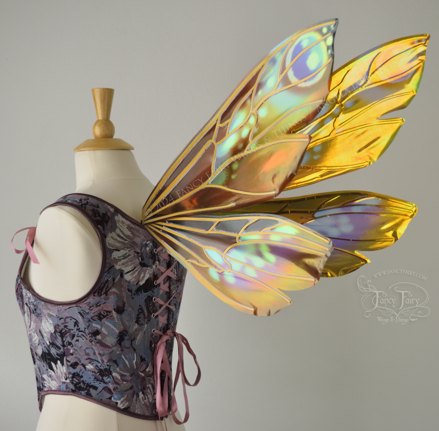 Wasp-shaped iridescent fairy wings in warm orange & rust colors with touches of blue, purple and pink, worn on a dress form, back 3/4 view