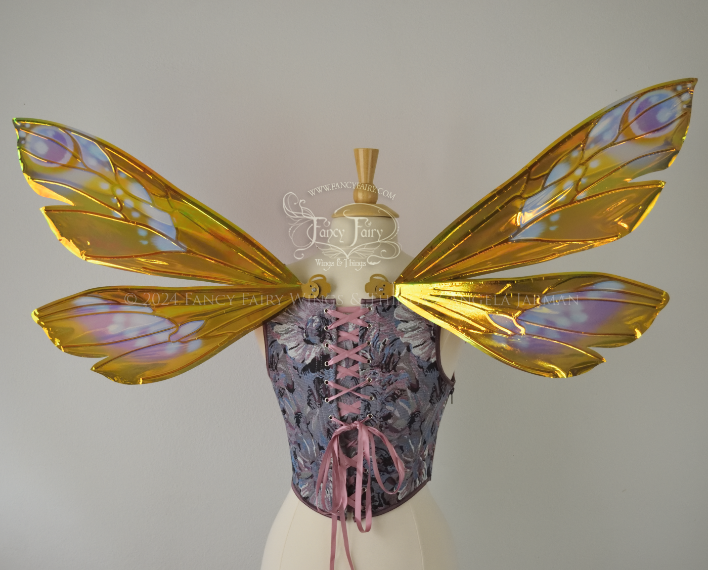 Wasp-shaped iridescent fairy wings in warm orange & rust colors with touches of blue, purple and pink, worn on a dress form, back view