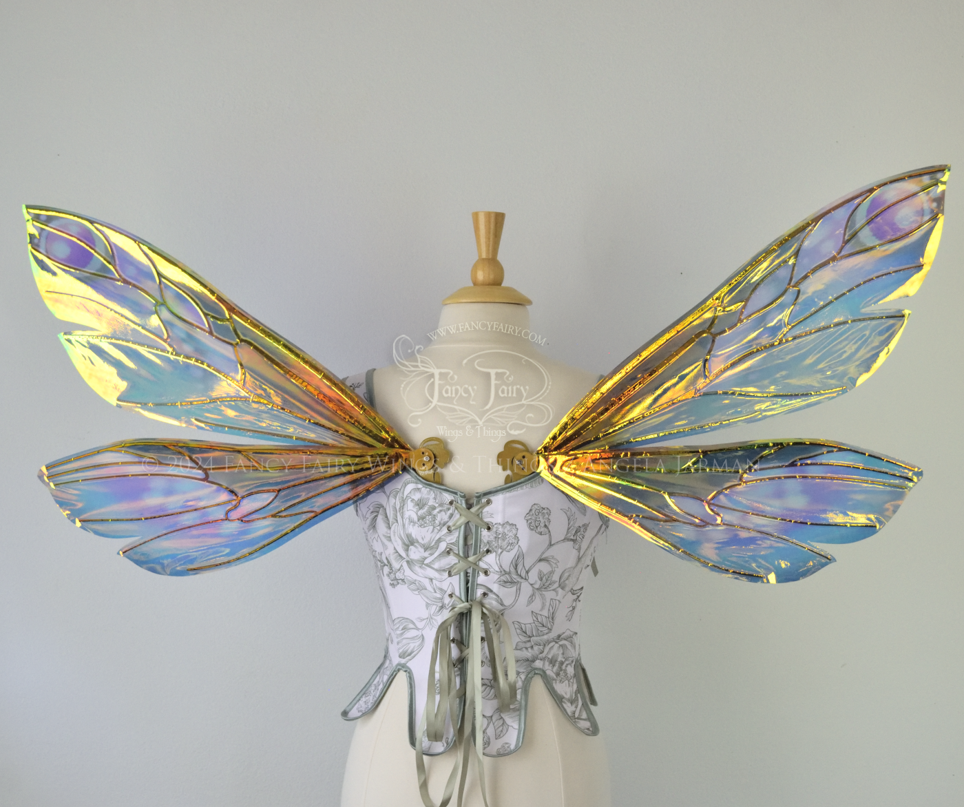 Back view of iridescent fairy wings in various shades of green, teal, blue, lavender with touches of pink, with gold veins, worn on a dress form with white & green corset